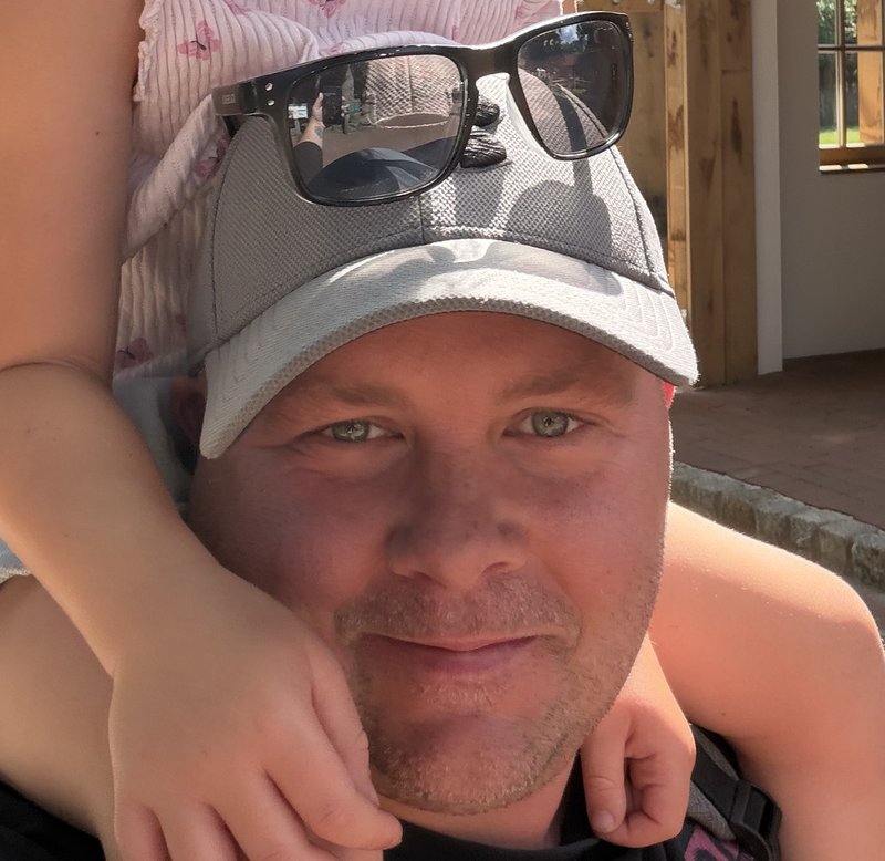 Thomas mit Basecap und Sonnenbrille, auf seinen Schultern sitzt seine Tochter – von ihr sind nur die Arme zu sehen